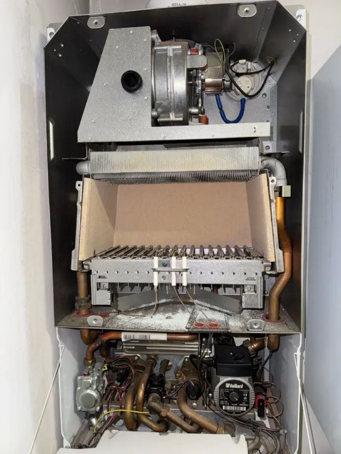 Photo d’une chaudière ouverte avec le brûleur en cours d’entretien. On y voit clairement les composants internes, notamment le brûleur, les conduites et les éléments de sécurité. L’image illustre une opération de maintenance professionnelle, mettant en avant la propreté et la sécurité de l’appareil. Idéal pour un site spécialisé dans le chauffage, l’entretien des chaudières et la maintenance énergétique.